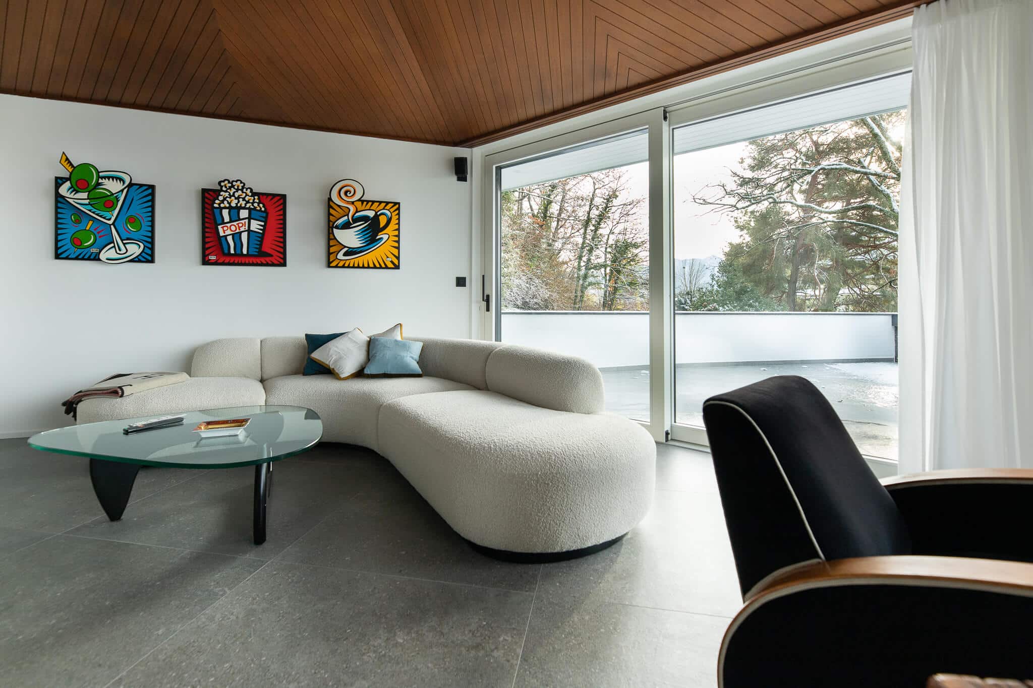 Séjour d'un appartement rénové à Montreux. Carrelage gris et peinture blanche. Mobilier design devant peinture pop art.