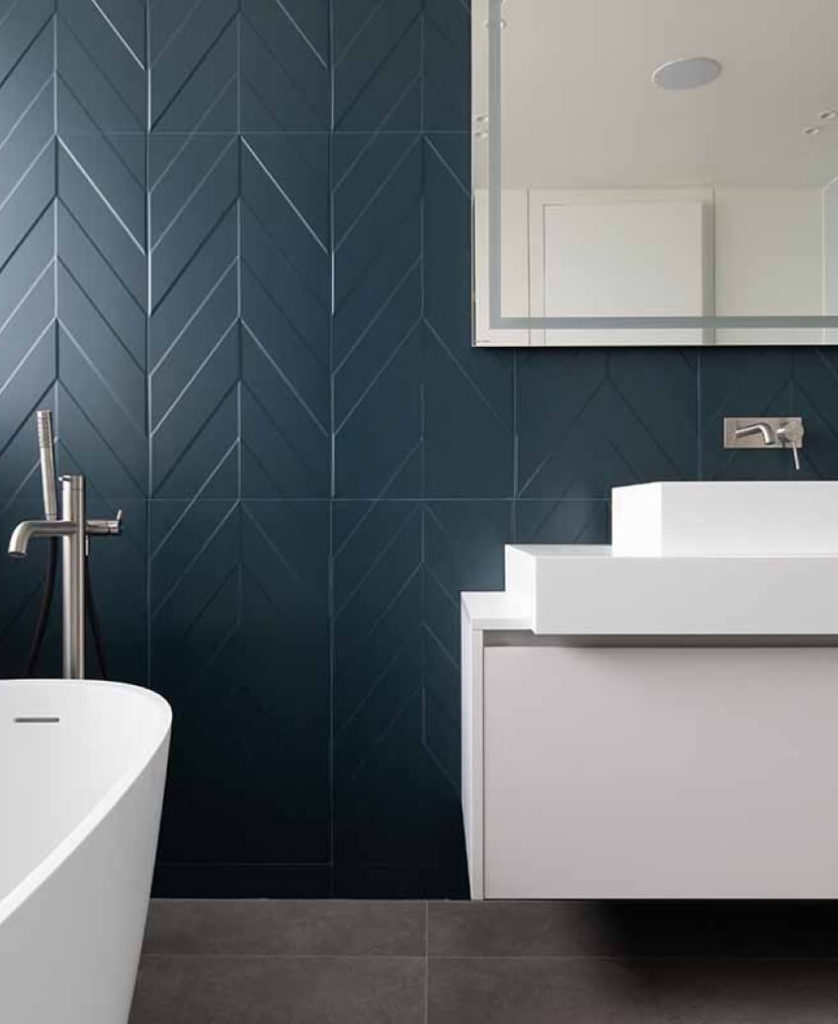 Mur de salle de bains avec carrelage en chevrons bleu. Baignoire et lavabo moderne de couleur blanche 