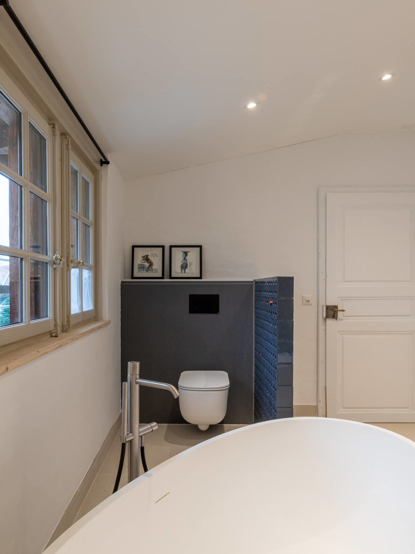 Robinet de baignoire argenté devant petit espace de toilette avec carrelage gris et mur en brique peint et mur de couleur blanche