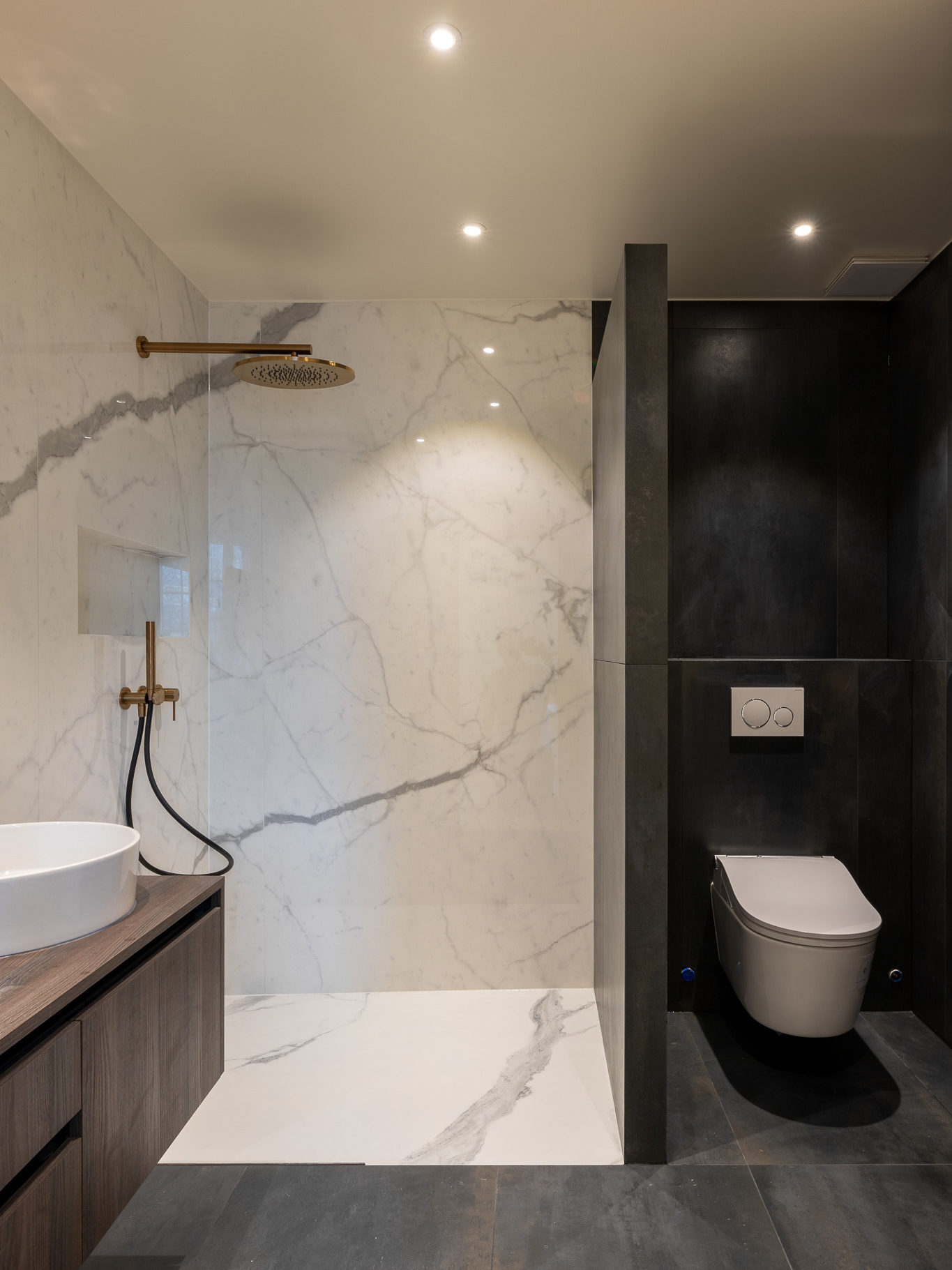 Salle de bains rénovée avec différenciation des espaces douches et WC. Carrelage imitation marbre pour la douche italienne et carrelage noir pour les WC.