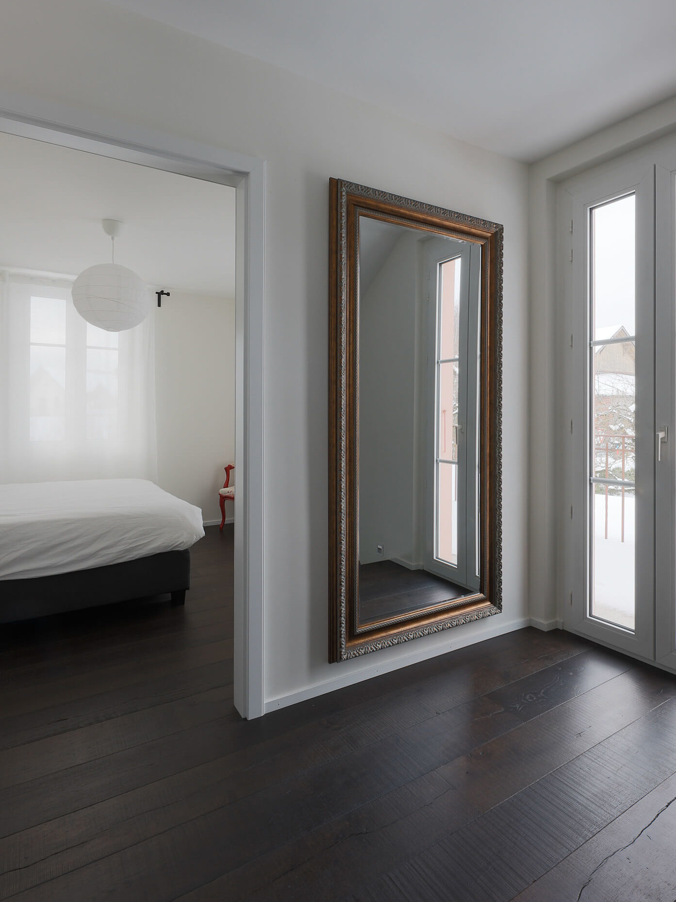 Couleur dans une maison rénovée à Savigny. Grand miroir devant une fenêtre et chambre d'invité en fond avec mobilier blanc