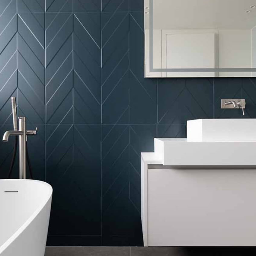 Mur de salle de bains avec carrelage en chevrons bleu. Baignoire et lavabo moderne de couleur blanche