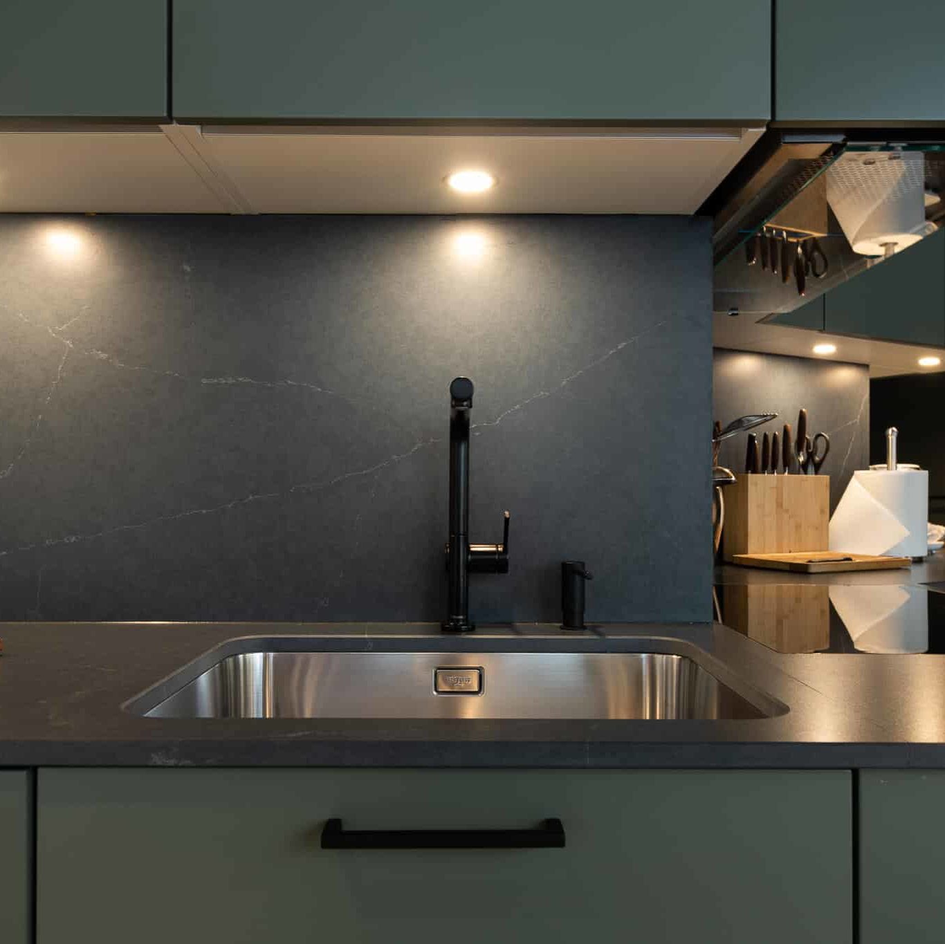 Evier moderne et robinet noir devant carrelage imitation marbre. Rénovation de cuisine à Montreux avec choix de mobilier de cuisine vert et plan de travail noire.