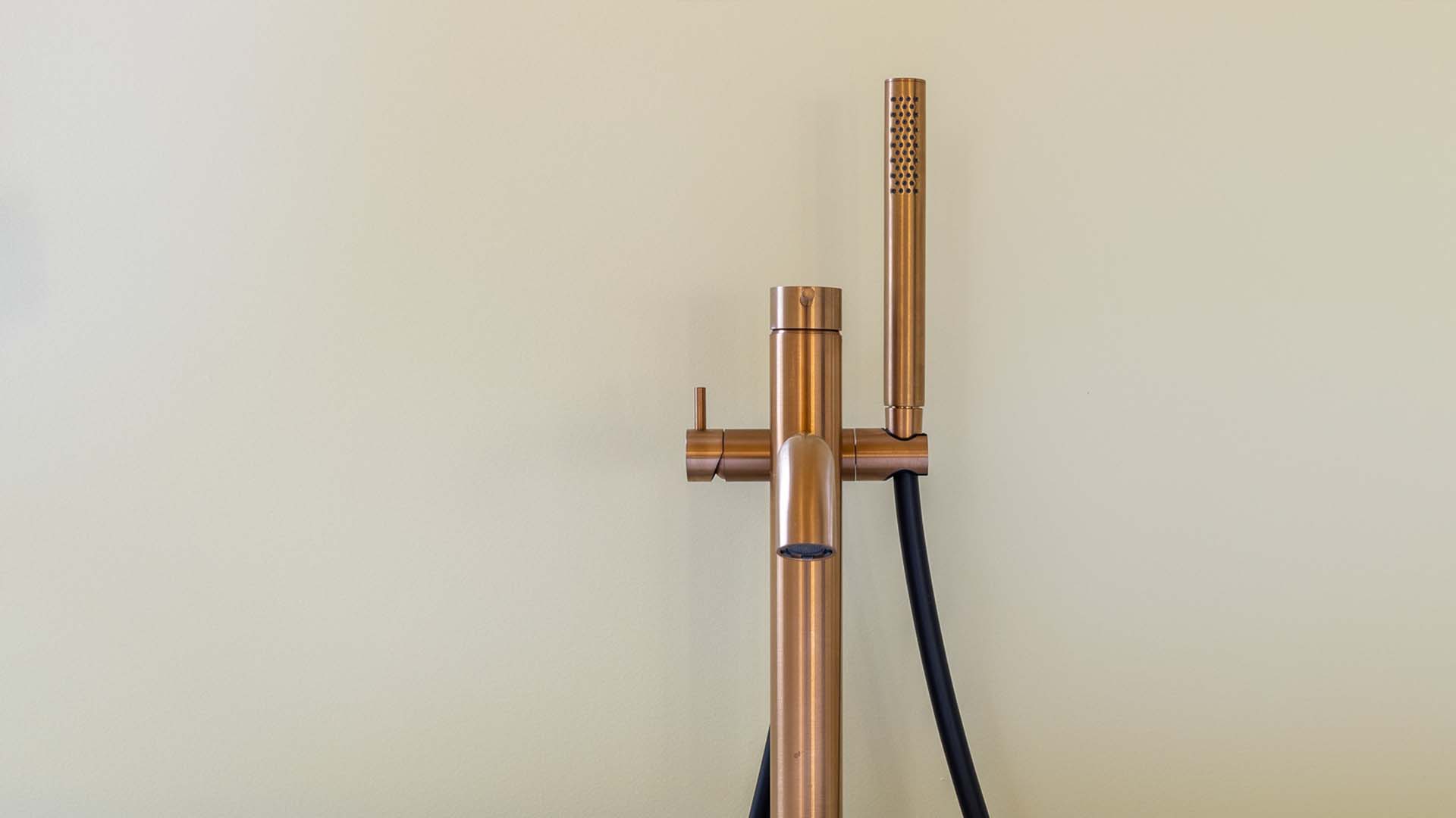 Robinet de baignoire et pommeau de douche doré devant mur
